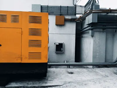 Orange industrial generator unit beside a building.