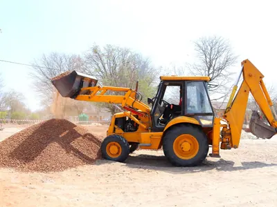 Yellow backhoe loader lifting soil on an open site.