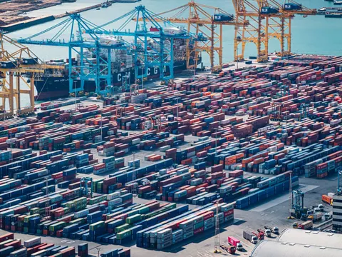 Aerial view of a container port with stacked shipping containers and cranes along the quay.